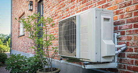 an air source heat pump installed onto the wall of a brick home